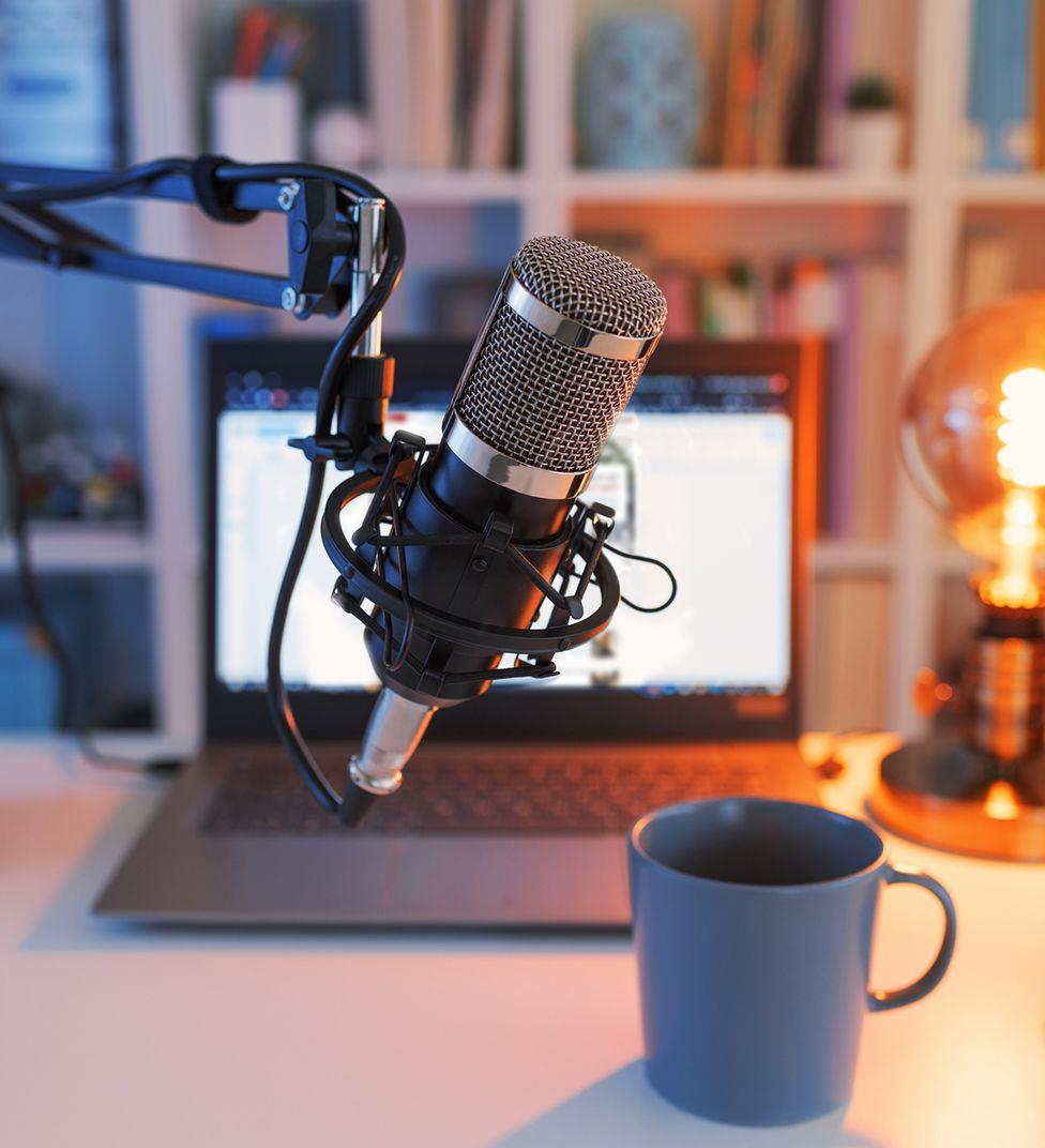 A podcast microphone in front of a laptop and a coffee mug